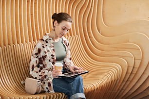 Graphic portrait of young professional using tablet while working at modern office space with designer chairs, copy space