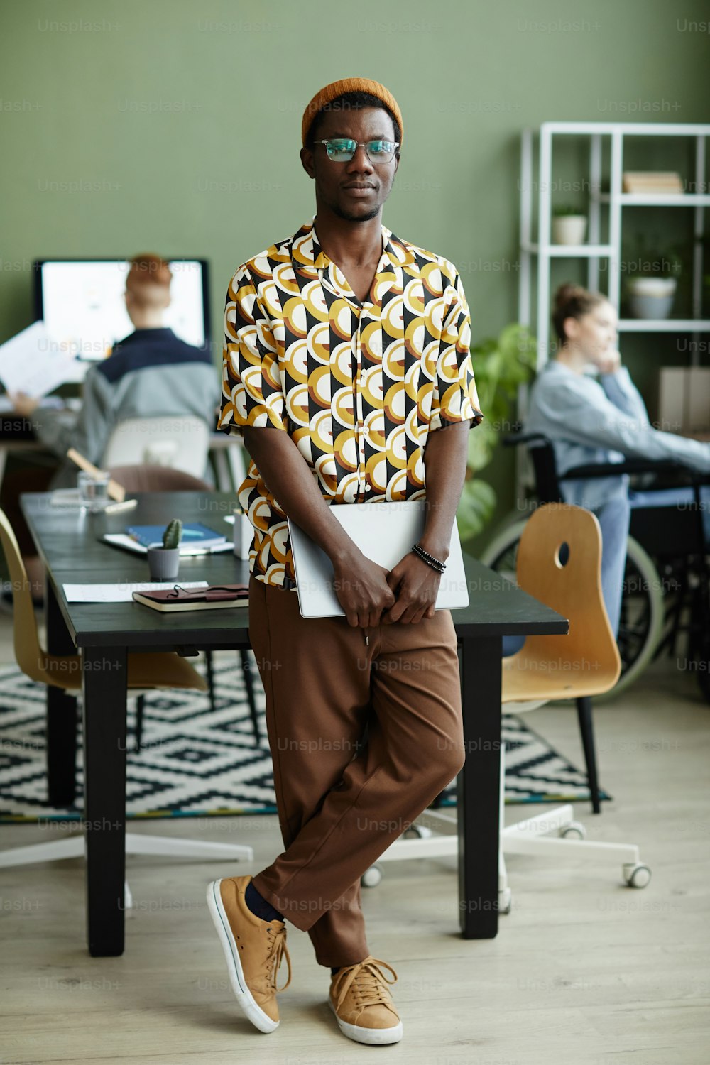Full length portrait of black young man wearing bright yellow pattern and looking at camera while standing in office