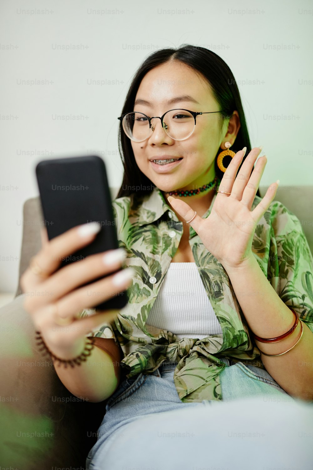 Retrato vertical de adolescente asiática saludando a un teléfono inteligente llegó mientras chateaba por video con un amigo iluminado por luz de neón
