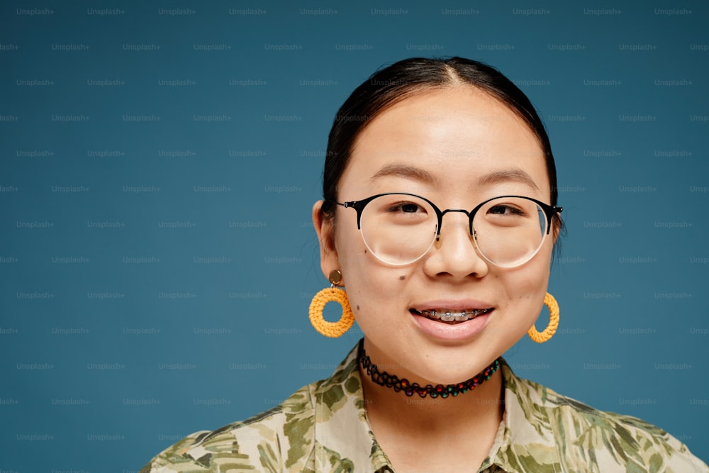 Minimales Porträt eines asiatischen Teenager-Mädchens, das eine Zahnspange trägt und in die Kamera über blauem Hintergrund schaut, Kopierraum