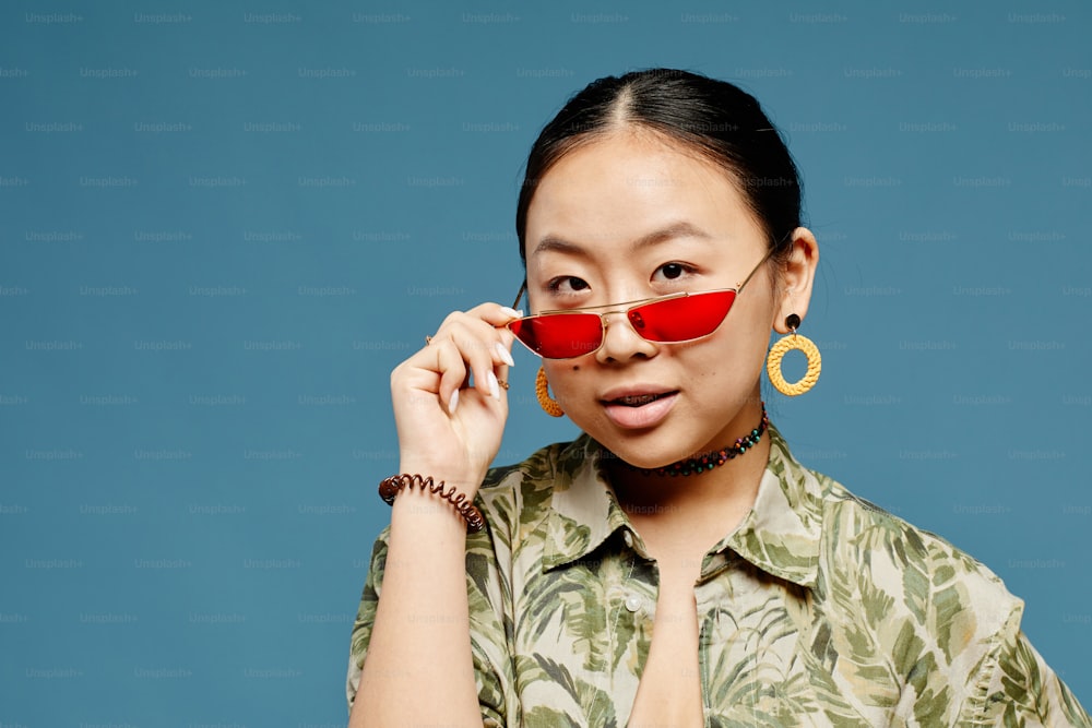 파란색 배경 위에 트렌디한 색의 선글라스를 끼고 있는 아시아 십대 소녀의 미니멀 초상화, 복사 공간