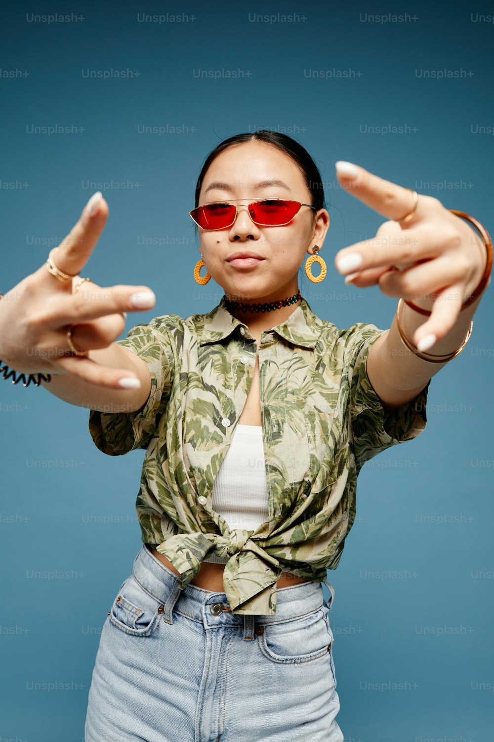 Vertical portrait of trendy teenage girl wearing colored sunglasses and gesturing over blue background