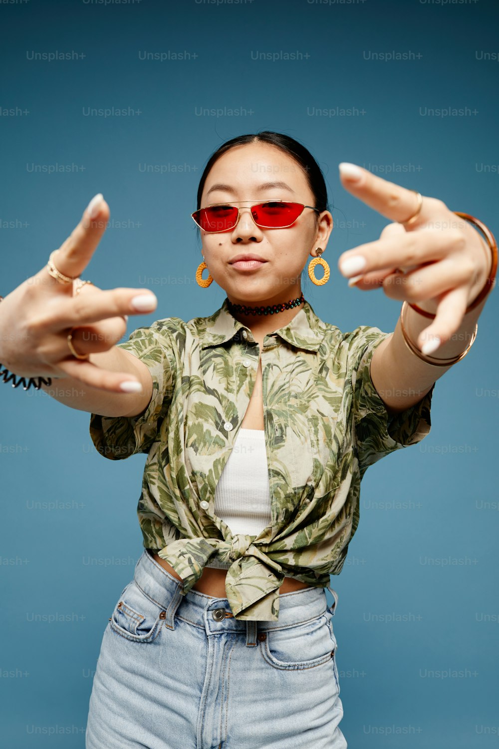 Vertical portrait of trendy teenage girl wearing colored sunglasses and gesturing over blue background
