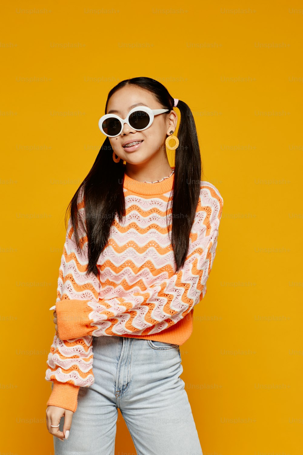 Vertikales Porträt eines asiatischen Teenager-Mädchens mit weißer Sonnenbrille auf leuchtend gelbem Hintergrund