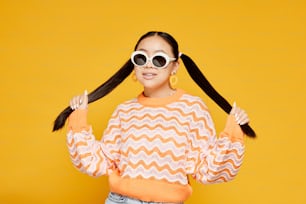 Waist up portrait of funky teenage girl with pigtails over colored yellow background, copy space