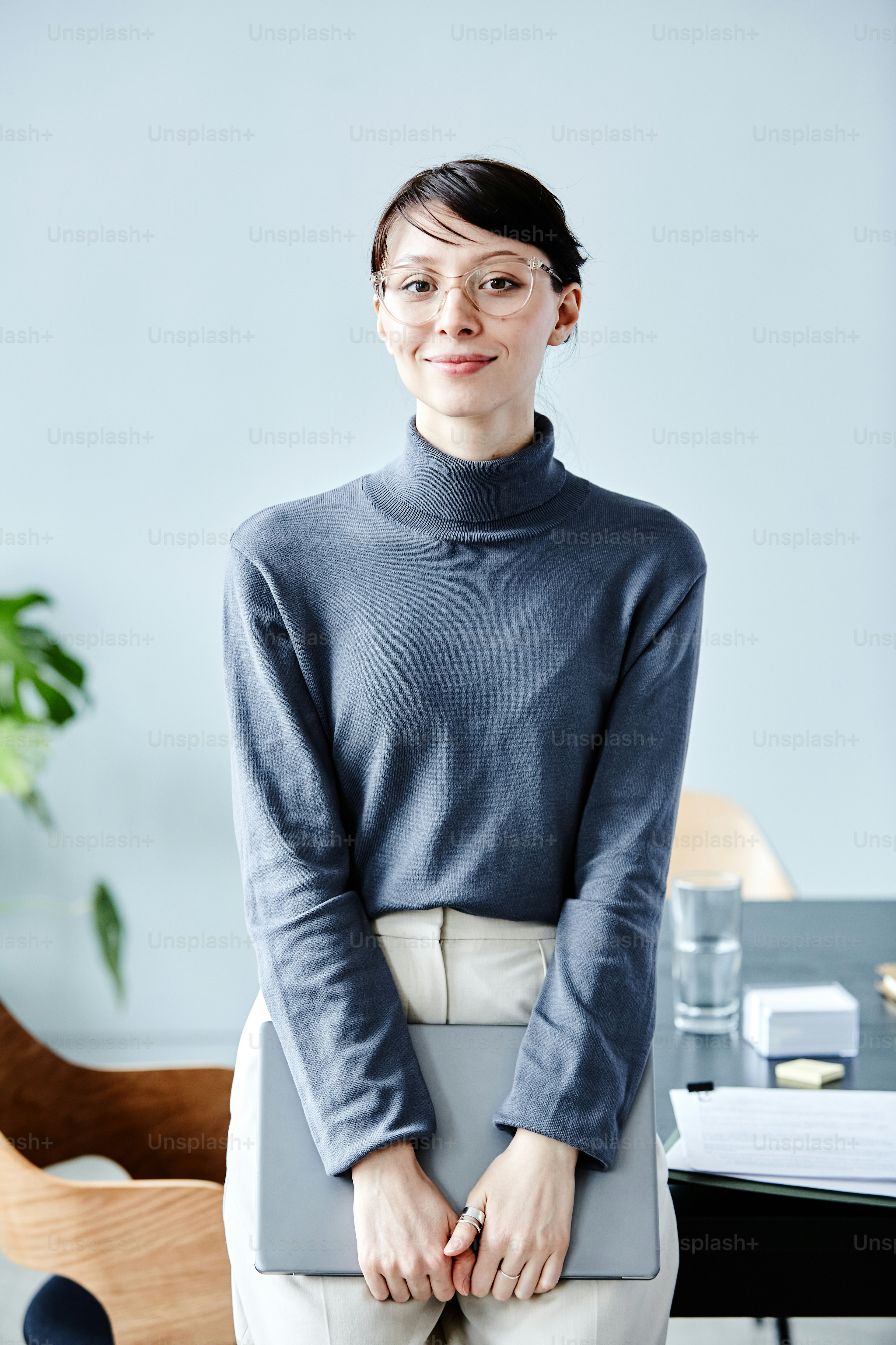 Minimal portrait of young businesswoman wearing glasses and smiling at camera while standing in office against blue