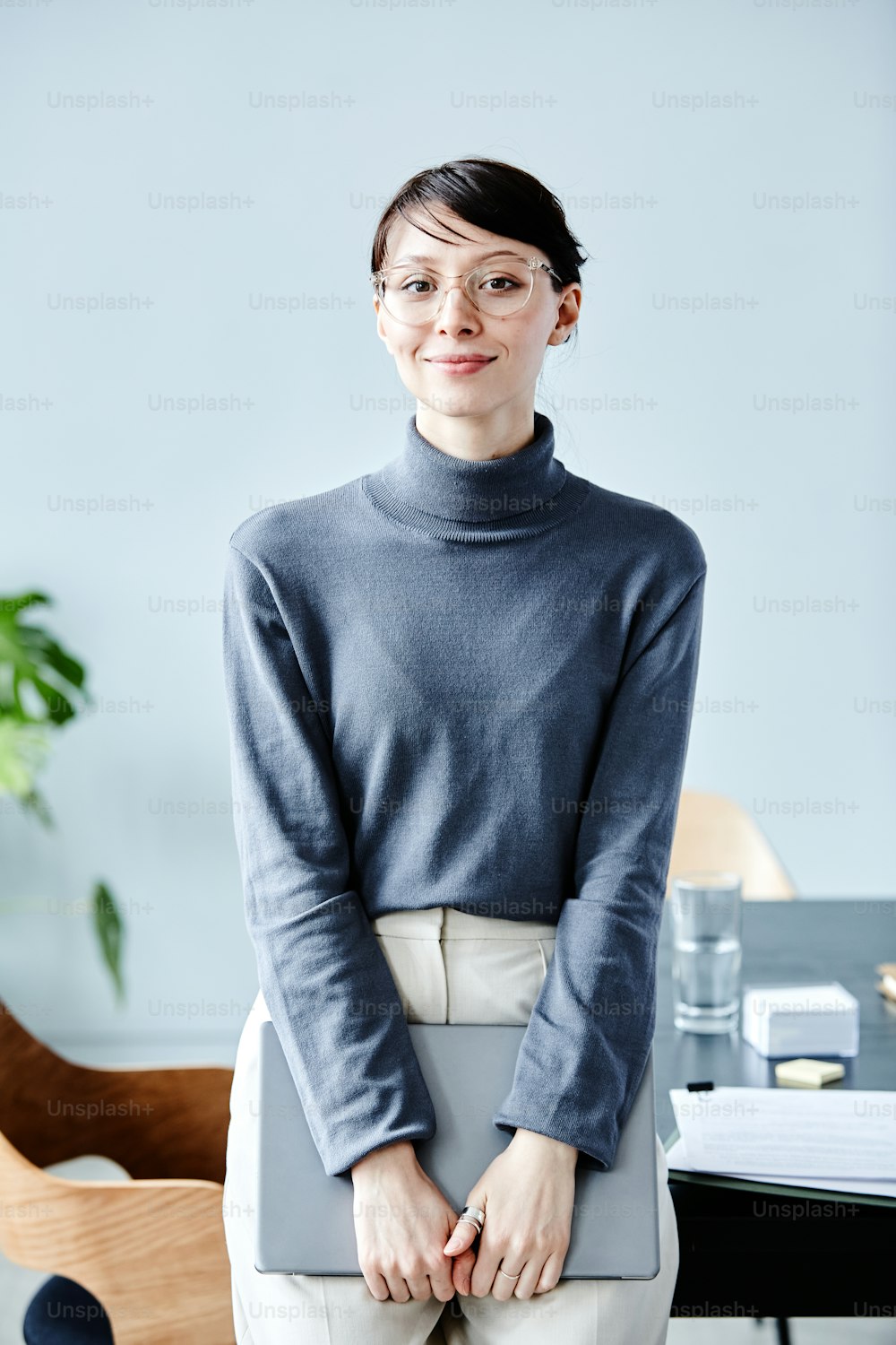 Minimal portrait of young businesswoman wearing glasses and smiling at camera while standing in office against blue
