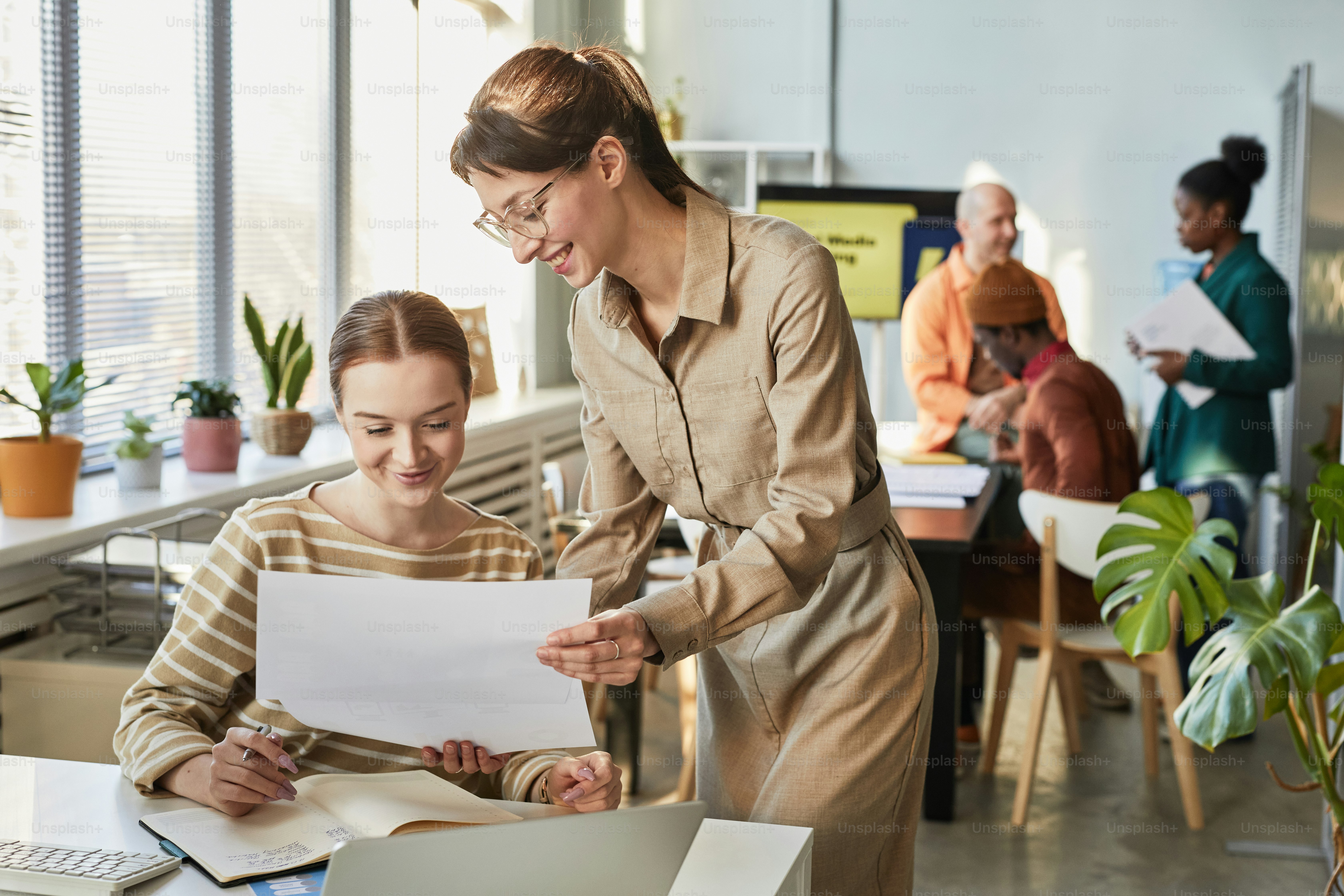 Portrait of two young business women discussing plan in office and smiling, copy space