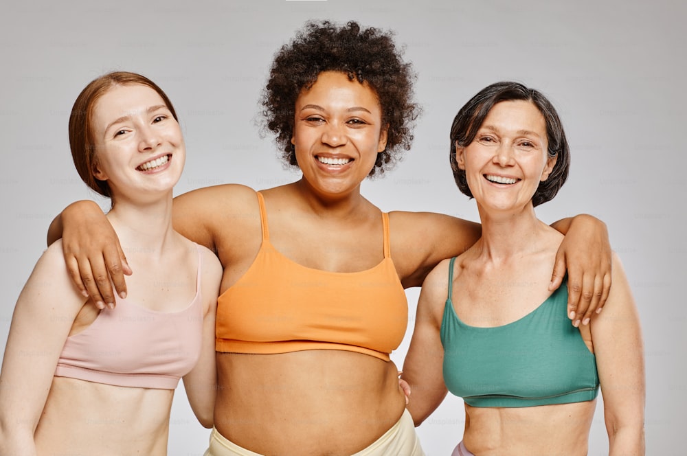 Minimale Taille nach oben, vielfältige Gruppe von echten Frauen, die Unterwäsche tragen und glücklich vor grauem Hintergrund lachen