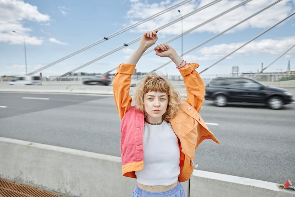 Ritratto in vita di giovane donna libera che indossa vestiti colorati sul ponte della città e guarda la macchina fotografica, spazio di copia