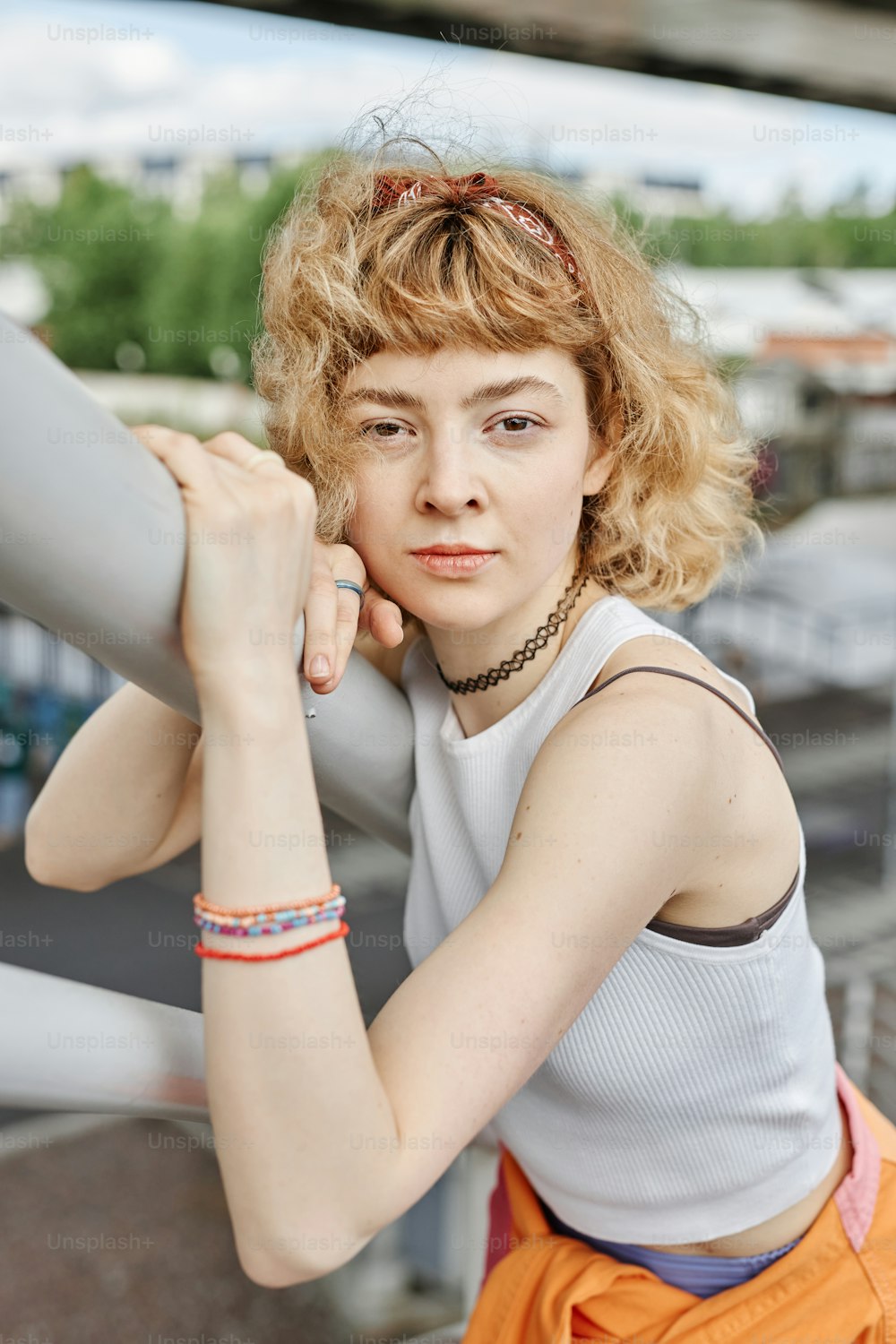 Candid portrait of young woman with curly hair looking at camera outdoors and wearing trendy outfit
