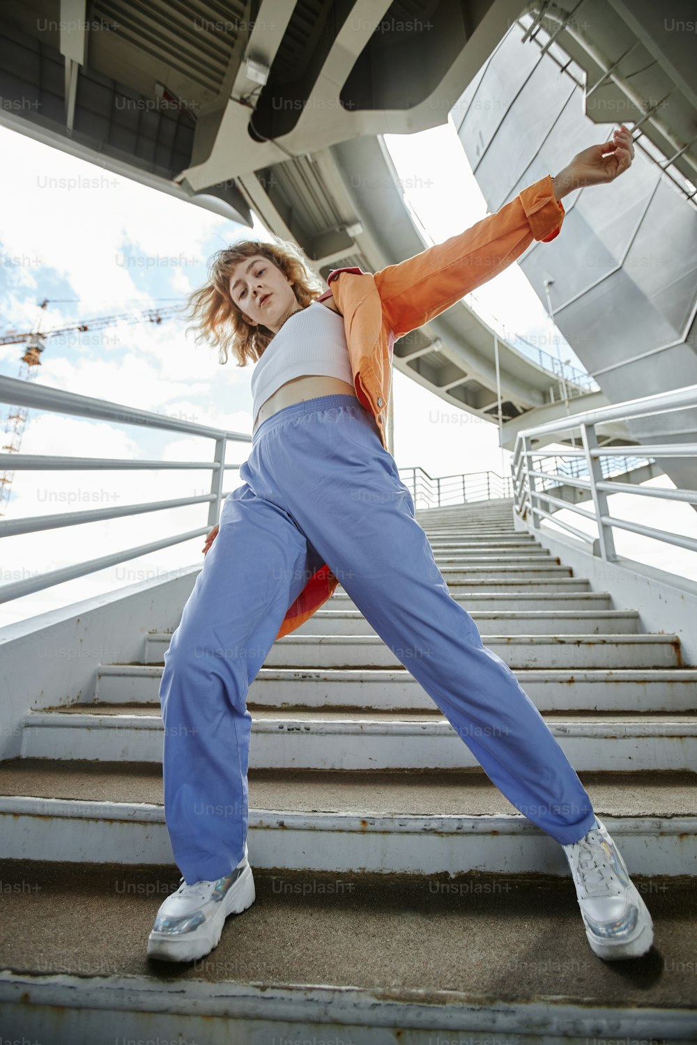 Dynamic full length shot of young woman dancing outdoors in urban area and wearing streetwear