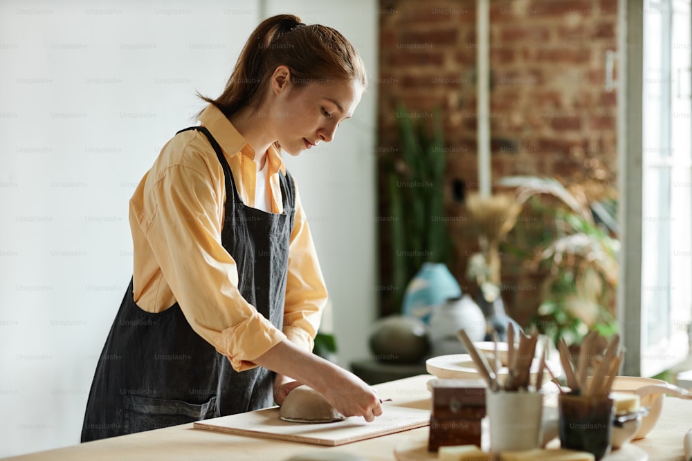 Side view portrait of young woman creating handmade ceramic bowl in cozy pottery studio, copy space
