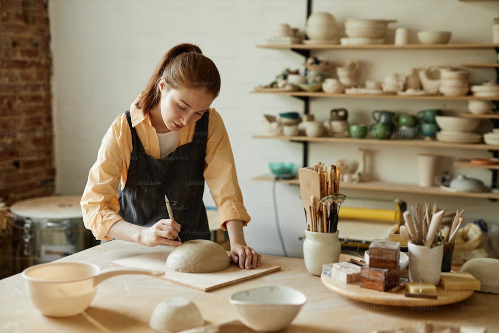 Warm toned portrait of young female artist shaping handmade ceramic bowl in pottery studio, copy space