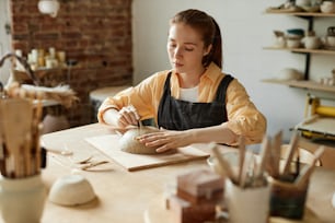 Warm toned portrait of young female artisan creating handmade ceramics in pottery workshop, copy space