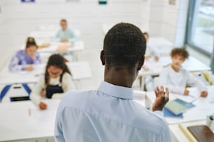 Minimal back view of male teacher taking to diverse group of kids in class