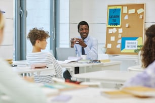 Ritratto dell'uomo nero sorridente come insegnante con i bambini in classe, spazio di copia