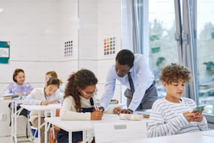 Ritratto di insegnante maschio nero che lavora con i bambini che fanno il test in classe scolastica