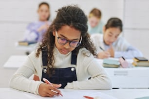 Porträt eines jungen schwarzen Schulmädchens, das am Schreibtisch im Klassenzimmer der Schule sitzt und einen Test macht