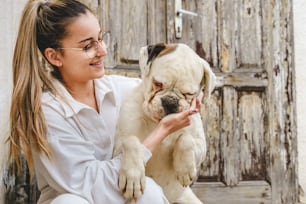 Giovane donna caucasica seduta sulle scale di fronte alla sua casa in giorno con il cane bianco che gioca con lui e si prende cura di - amicizia animale domestico concetto di amore persone reali foto brillante vista frontale copia spazio