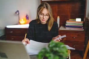 Uma jovem estudante caucasiana sentada em casa escrevendo e lendo em seu caderno segurando lápis enquanto estudava se preparando para o conceito de aprendizado e educação do exame pessoas reais copiam o espaço