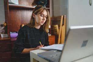 Una giovane studentessa caucasica seduta a casa a scrivere e leggere nel suo taccuino tenendo la matita mentre studia la preparazione per l'esame apprendimento e concetto di istruzione persone reali copiare lo spazio