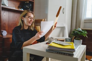 Una giovane donna studentessa caucasica seduta a casa tenendo la busta con la lettera di posta felice uscito sorridente lettura risultati del test di ingresso successo e concetto di realizzazione persone reali copia spazio