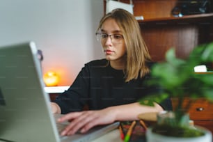 One young caucasian woman female student working on her laptop computer sitting at the table at home writing typing online learning and education concept checking test results or internet shopping