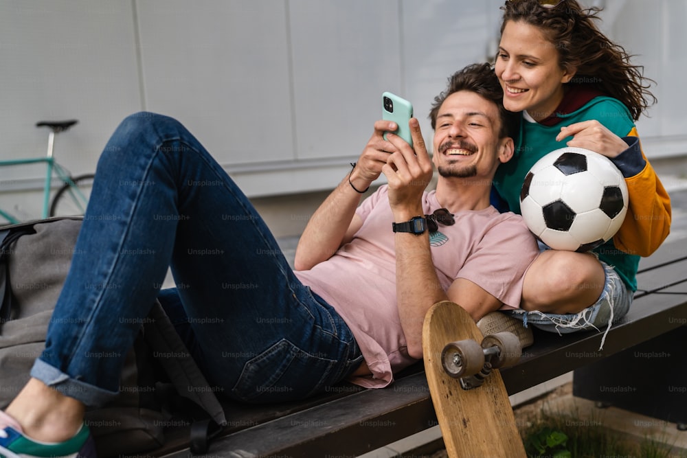 Couple woman and young caucasian man modern happy adult male and female boyfriend and girlfriend smile sitting in front of stadium holding soccer ball outdoor in day football game concept copy space
