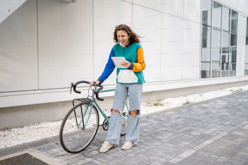 one woman young adult caucasian female walking by the modern building with her bicycle in day full length copy space female student in front of university casual lifestyle concept hold digital tablet