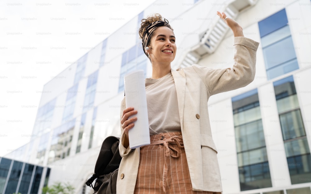 Uma jovem mulher mulher de negócios ou estudante verificando documentos em frente ao edifício moderno na universidade ou empresa em dia brilhante pessoas reais copiar espaço em pé sozinho segurar papel sorriso feliz
