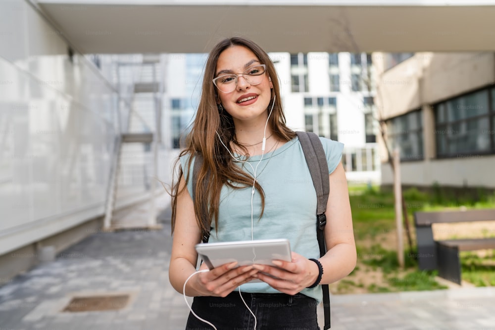 One woman young adult caucasian female student standing in front of university building outdoor in bright day using digital tablet waiting happy smile real people copy space