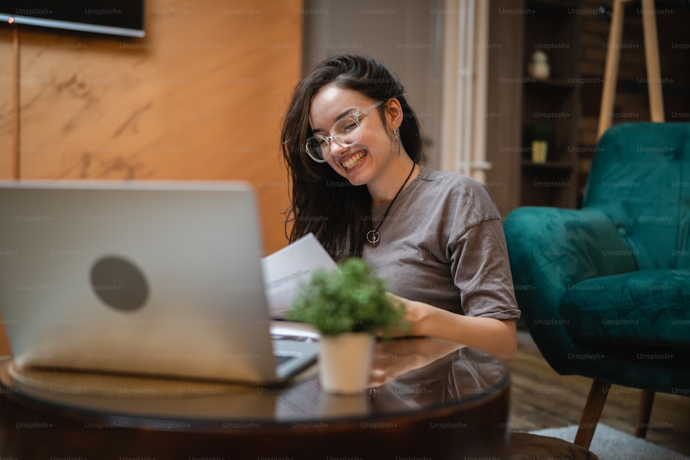 Front view on young caucasian woman study in front of the laptop computer at home - Girl reading book preparing exam test having online consultation - education and learning concept