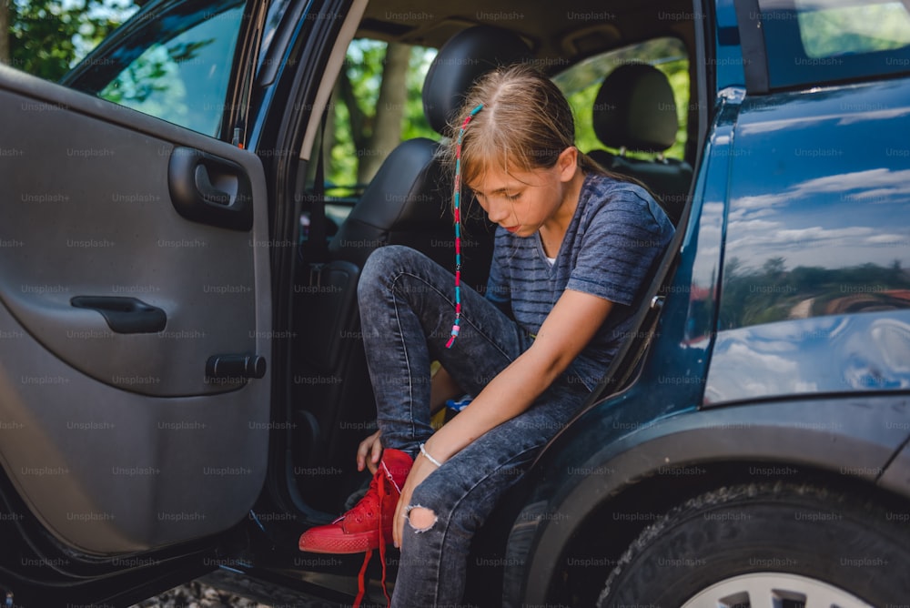 Little girl sitting in the car and putting on red sneakers