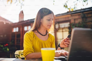 Women wearing yellow shirt sitting in the backyard patio, shopping online on laptop and using credit card