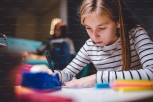 Girl sitting at coffee table in living room with her mother in the background and doing homework late at night