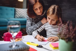 Girl sitting at coffee table in living room with her mother and doing homework late at night