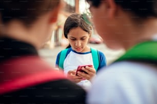 School girl wearing backpack using smart phone in the street