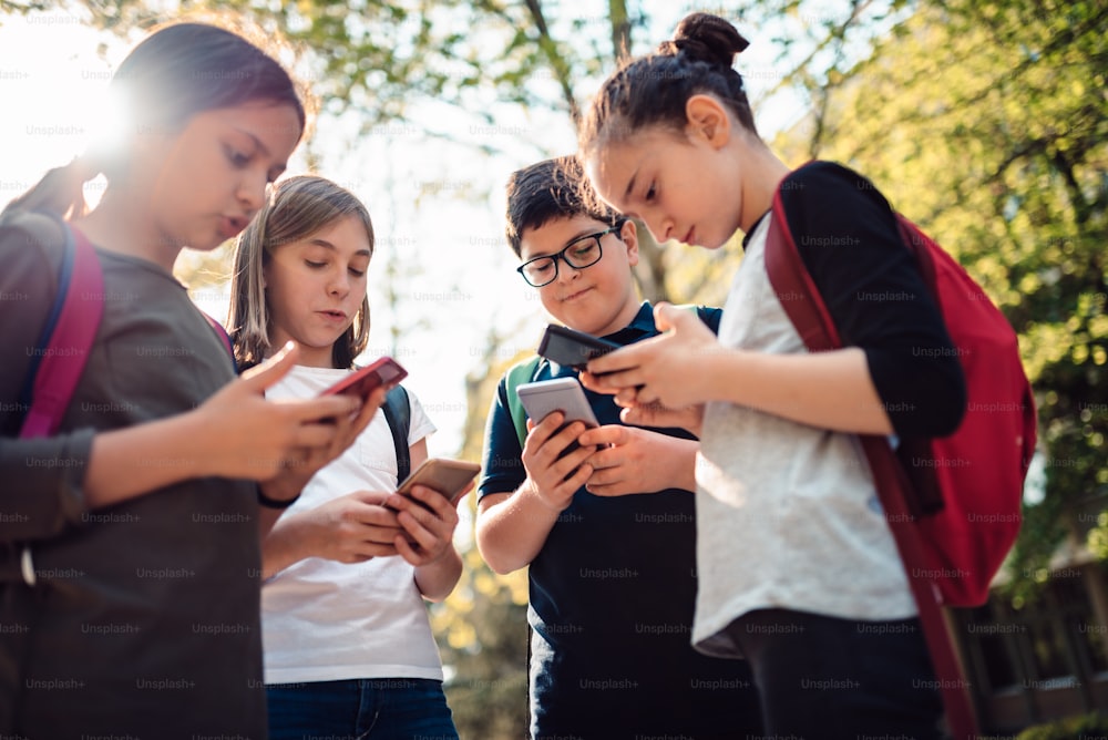 学校の子供たちのグループが路上でたむろし、スマートフォンを使う