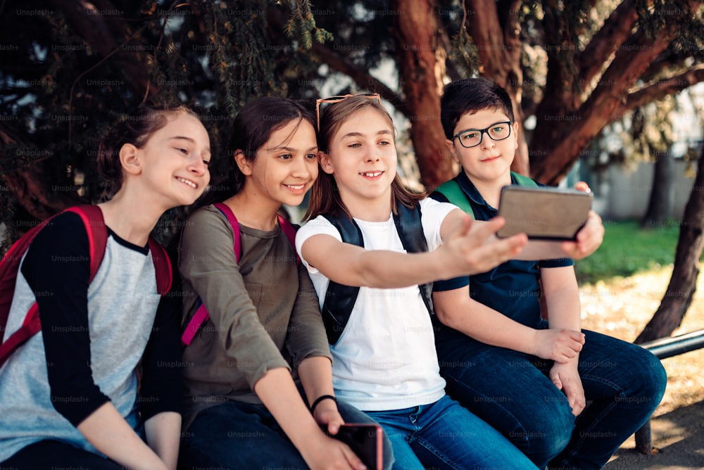 Klassenkameraden hängen nach der Schule im Schatten des Baumes ab und machen Selfies mit dem Smartphone