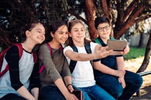 Los compañeros de clase pasan el rato a la sombra del árbol después de la escuela y se toman selfies con el teléfono inteligente