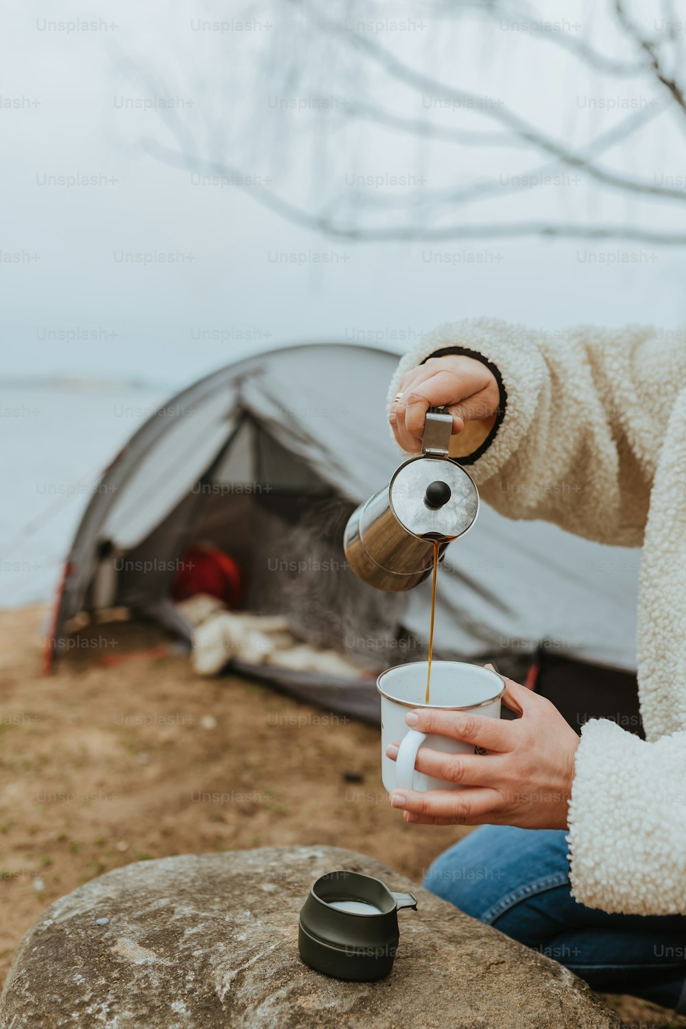 テン��トの前でカップにコーヒーを注ぐ人