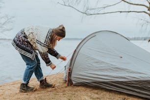 Une femme installant une tente à côté d’un plan d’eau