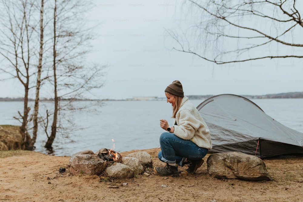 a woman sitting next to a tent next to a lake