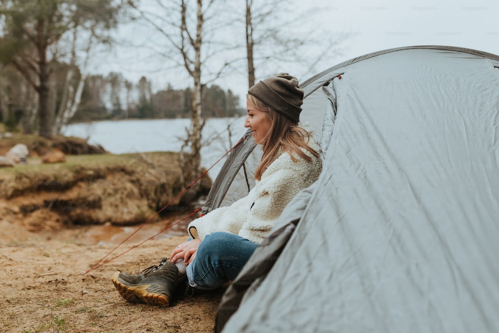 uma mulher sentada dentro de uma tenda ao lado de um lago