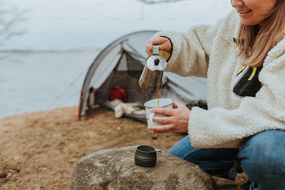 a woman pouring a cup of coffee in front of a tent