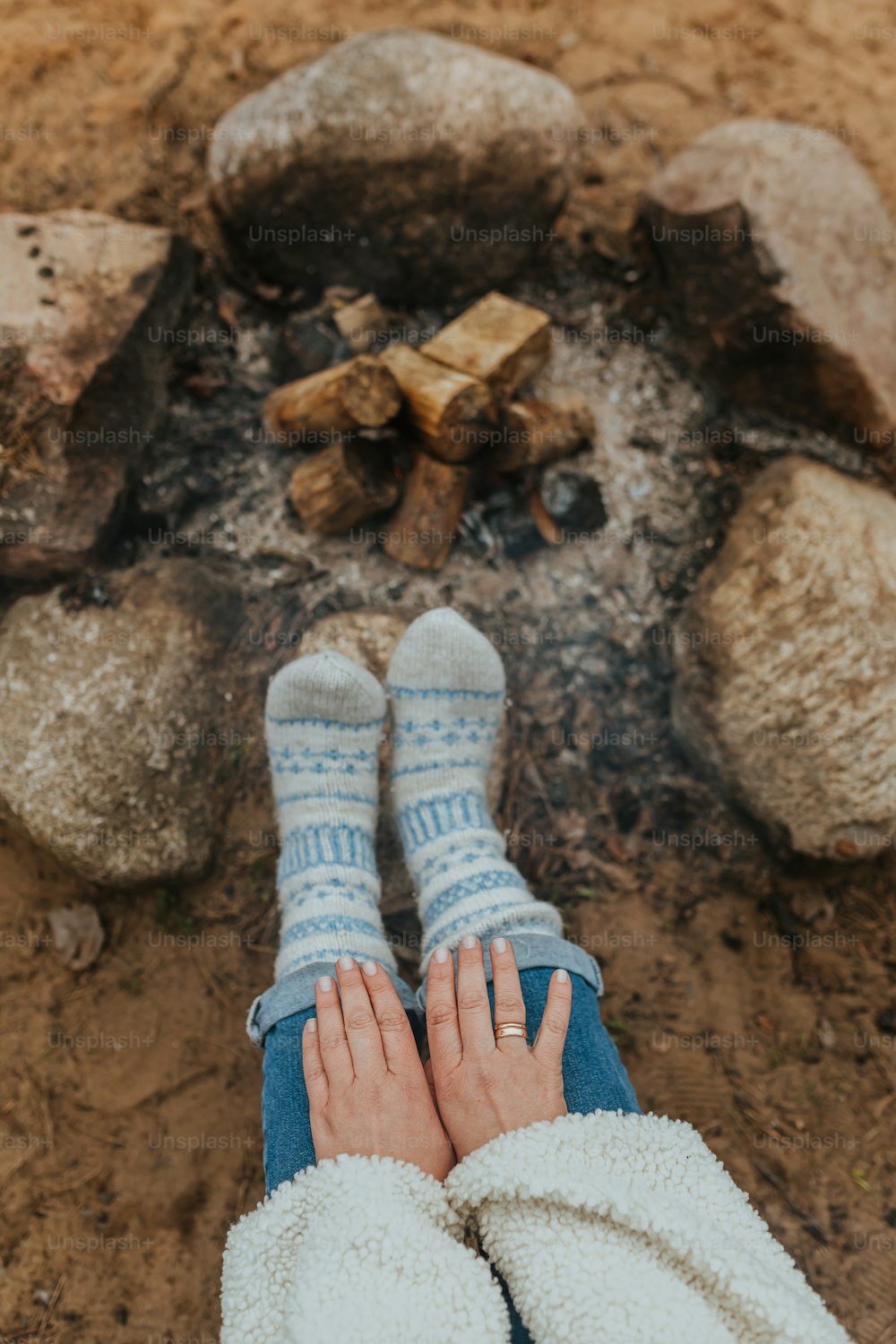 eine Person, die mit erhobenen Füßen vor einem Lagerfeuer sitzt