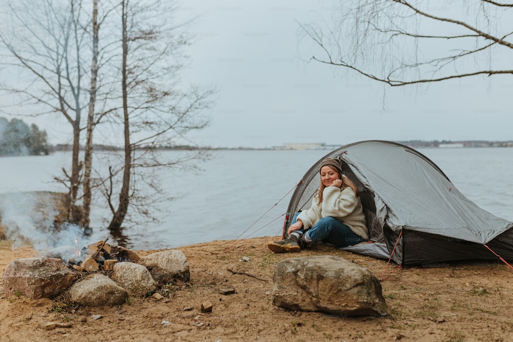 a woman sitting in a tent next to a lake