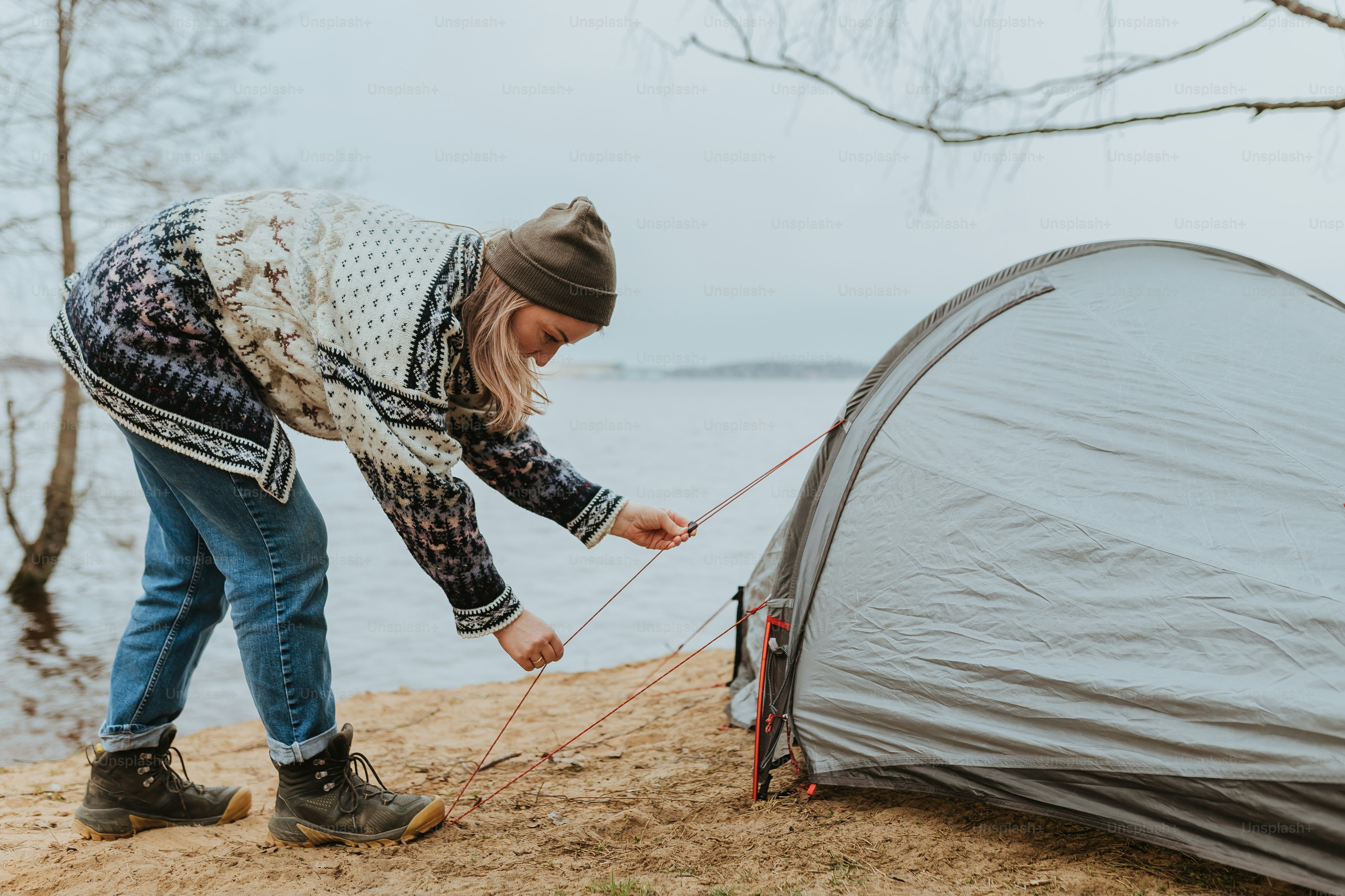 a woman putting up a tent next to a body of water