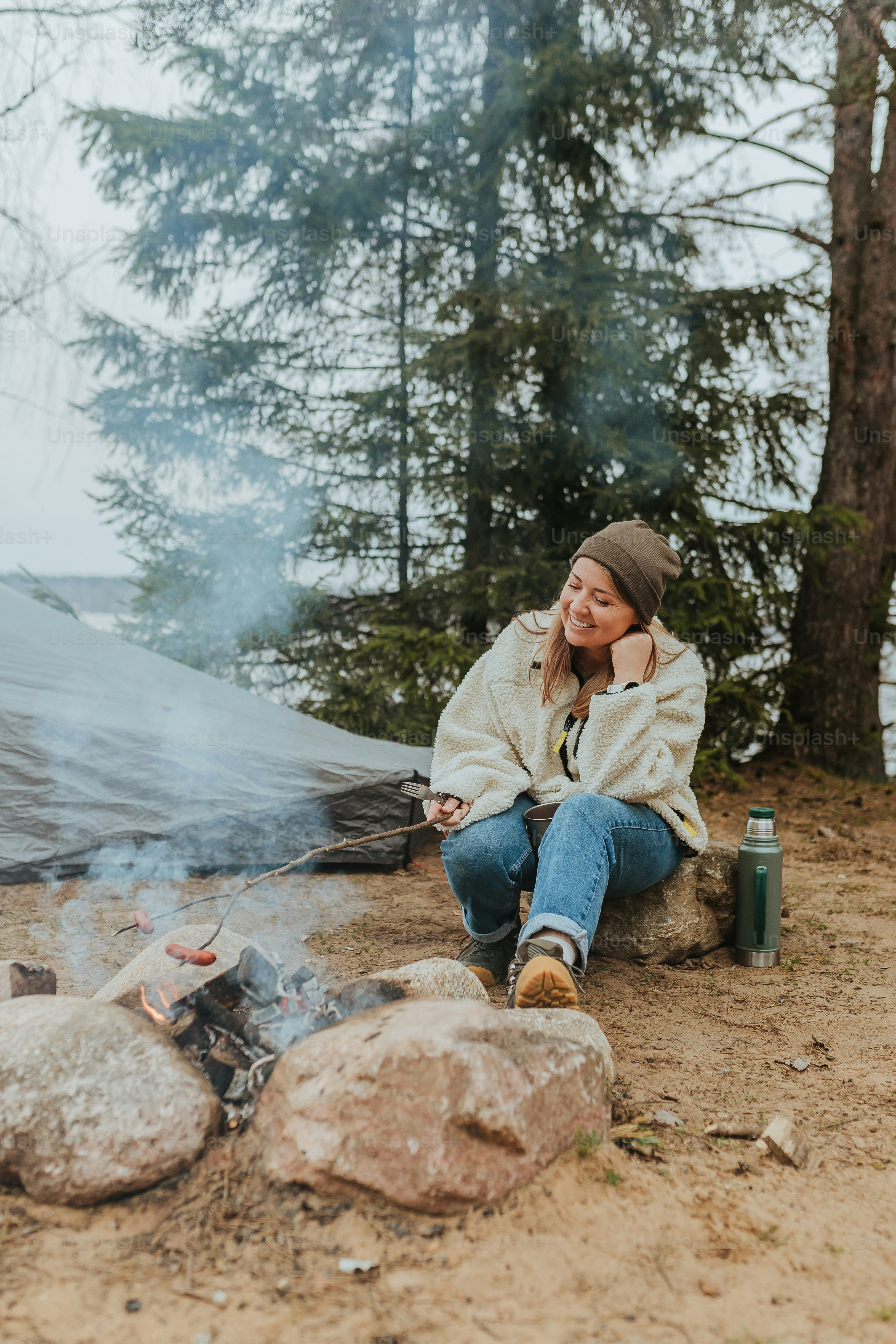 a woman sitting on a rock next to a campfire